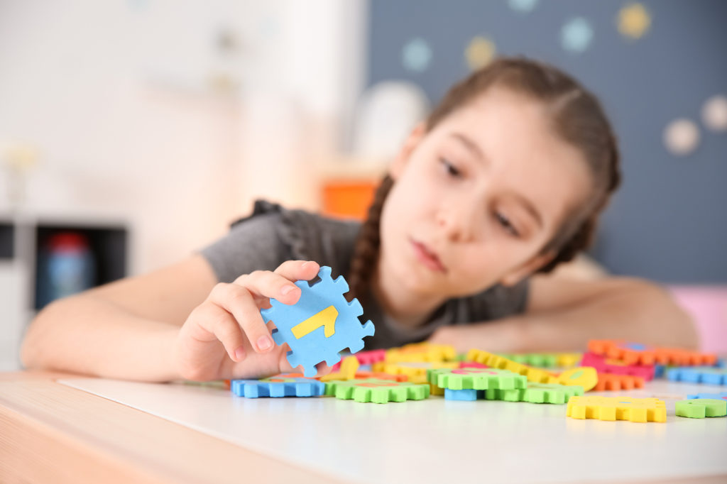 Little girl with autistic disorder playing at home, closeup of puzzles