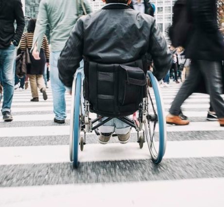 man in a wheelchair rolling through a pedestrian crossing surrounded by people walking in all directions